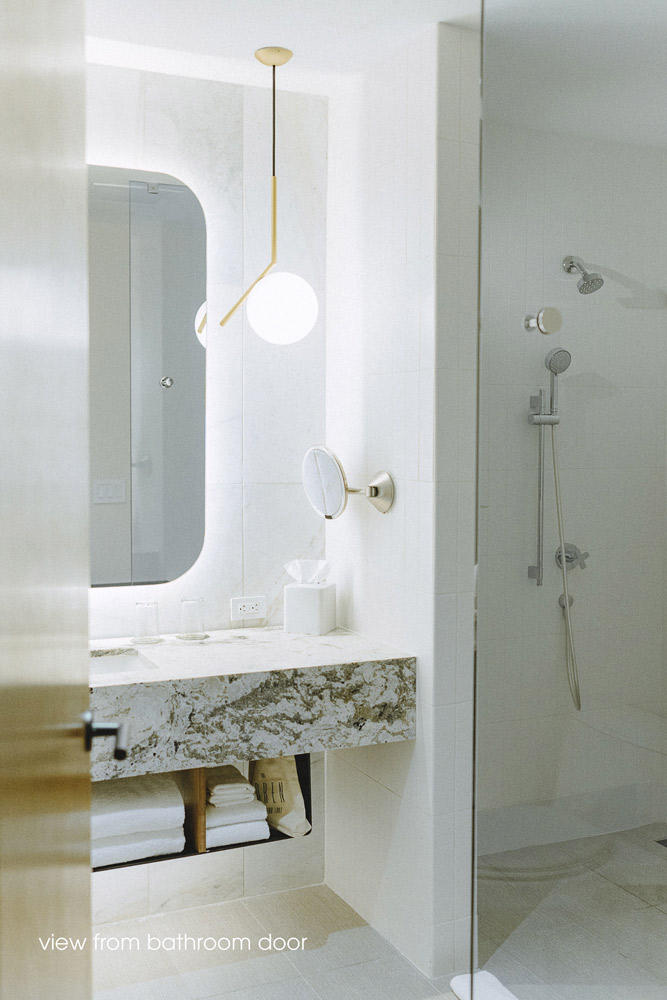 Batroom in white finishes with a marble floating vanity , backlit mirror above and a modern small pendant hangig by the mirror