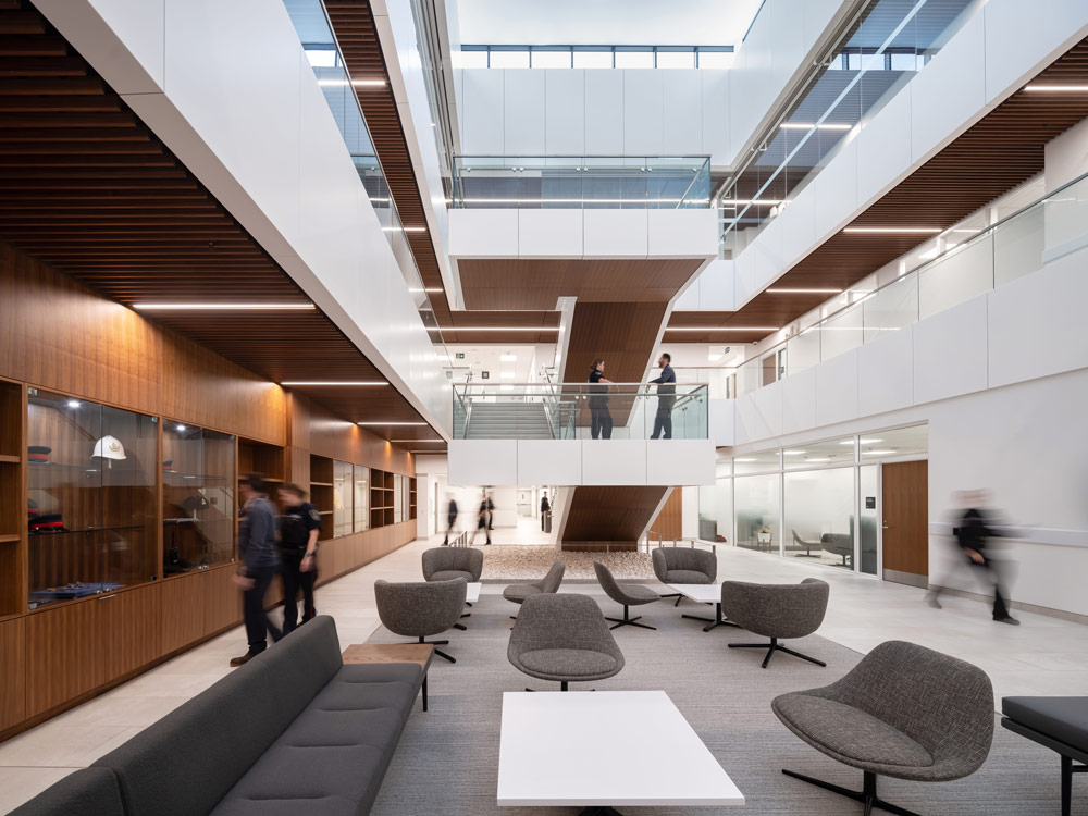 A view of the atrium from the seating area looking toward the large central staircase. On the left there is a wood paneled wall with built in glass cabinets displaying  items
