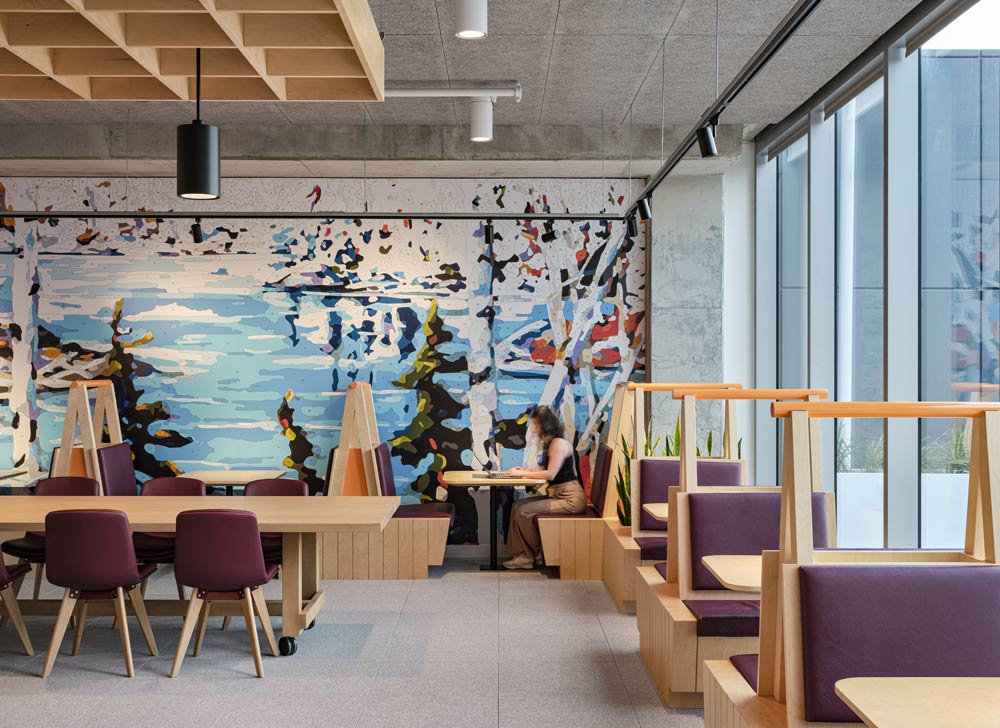 Canadian artwork as a mural in this space with seating booths placed along the mural wall and the adjacent floor to ceiling window. In the middle of the pace is a large table on wheels with chairs