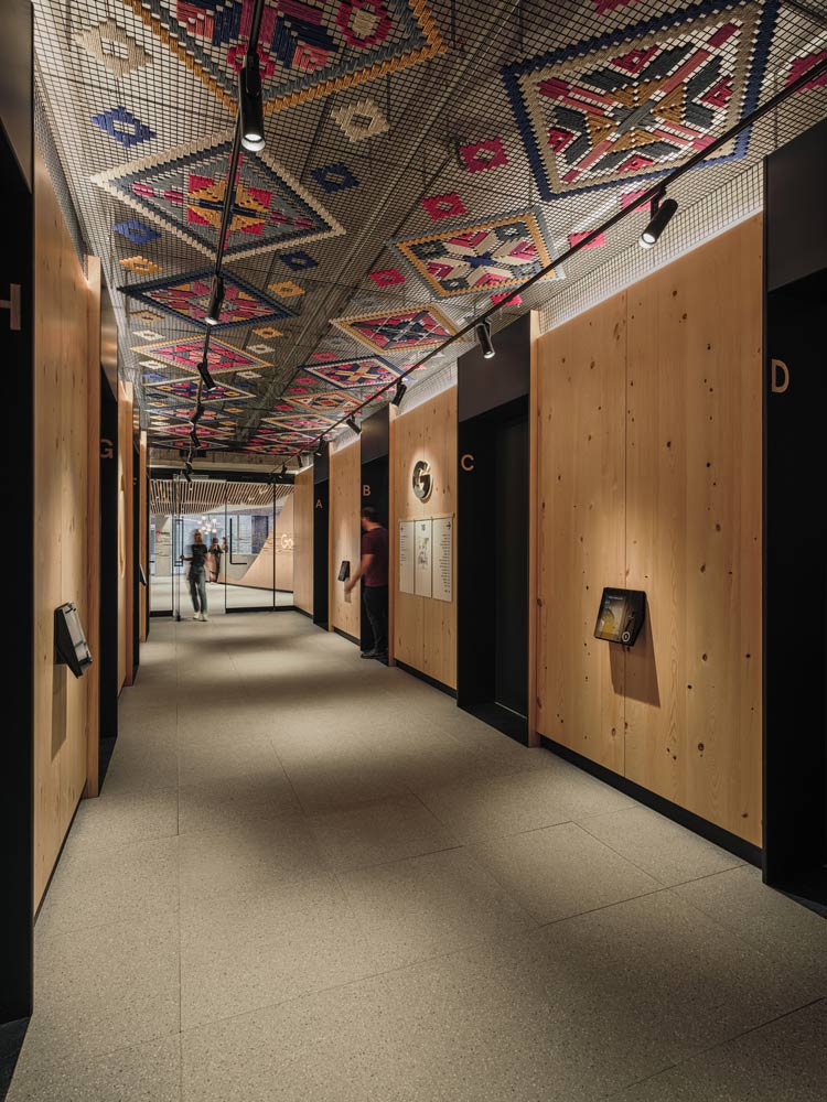 Elevator lobby with wood panelled walls, and an intricate colourful mosaic like ceiling featuring indigenous motifs