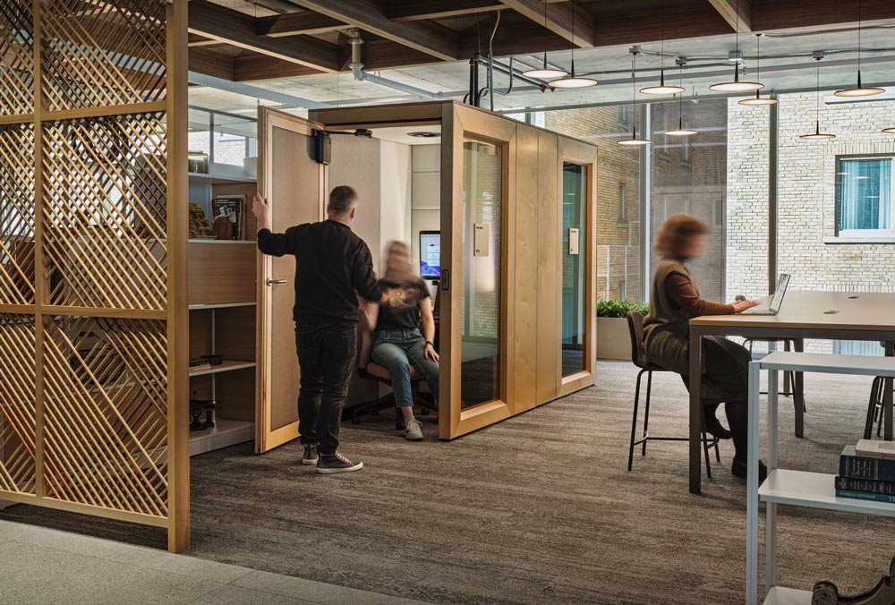 Private work pods and large tall desks are found within the common work area, separated by a wood dowel privacy screen