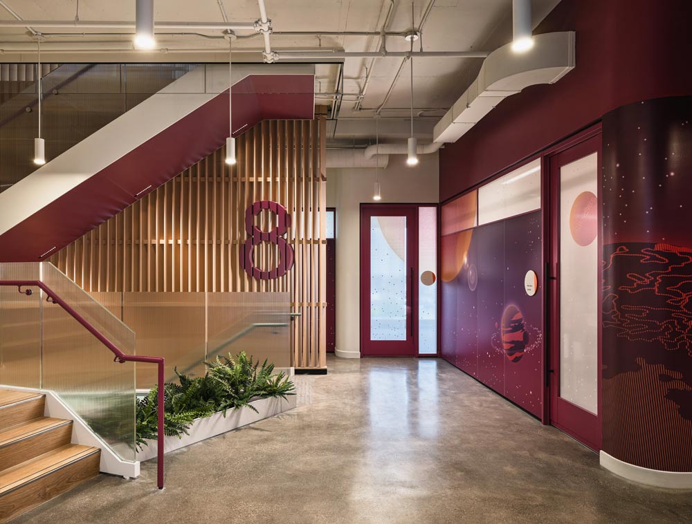 Hallway on 8th floor which is indicated on the feature wall with vertical wooden slats  right by the stairs, with a large maroon coloured no. 8. Across from the stairs on the right side of the photo is a maroon coloured wall with space motifs and planets