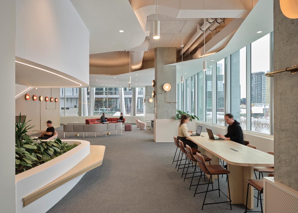 Wide open, well lit common area surrounded by large windows all around. lounge seating at the far end, and tall bar height tables with multiple stools on the right side, by the window