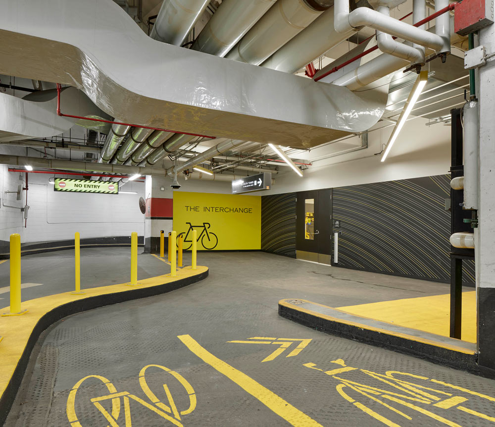 Entry way from the street with clearly defined bike lane drawn in yellow, against the gray walls, and a yellow wall with 'The Interchange' name written on it
