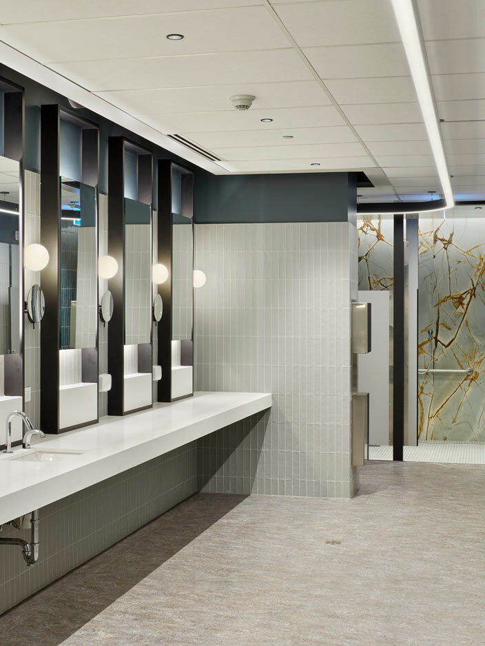 Accessible sink and counter with modern long vertical mirrors above. In the back of the space is the shower area