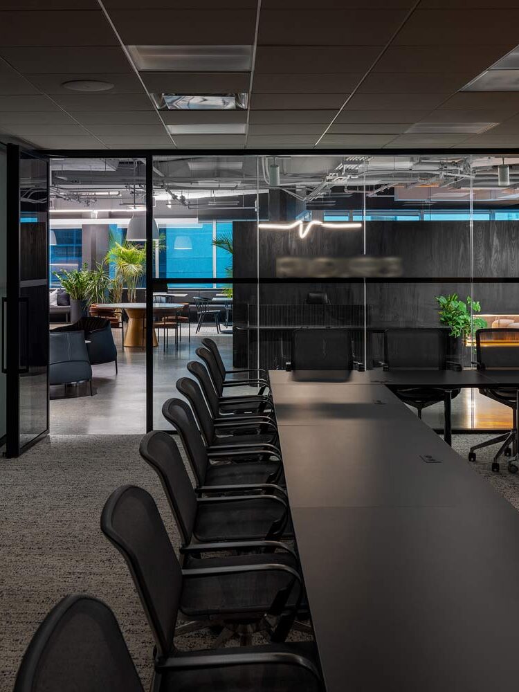 View from inside a board room with a long black table and black chairs toward a glass wall through which the reception area is visible.