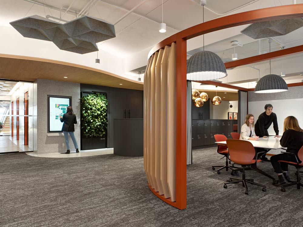 Work area with a large round desk and people working is separated from the hallway by a rounded privacy wall made of wooden vertical planks
