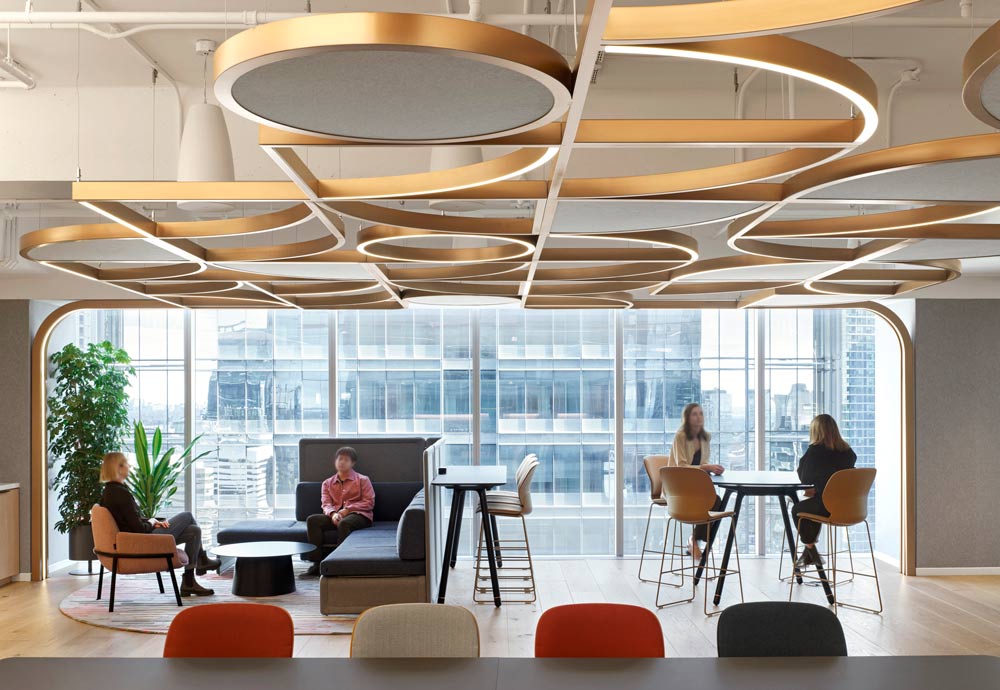 Common lounge and work area looking toward the floor to ceiling windows, with geometric detailing made of wooden strips on the ceiling