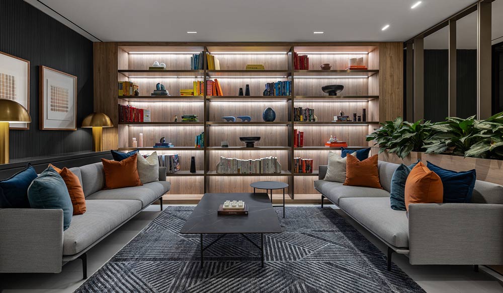 Cozy and comfortable living room-like seating area with two sofas facing each other and a backlit wall library adjacent to them, colourful details like pillows and books are throughout