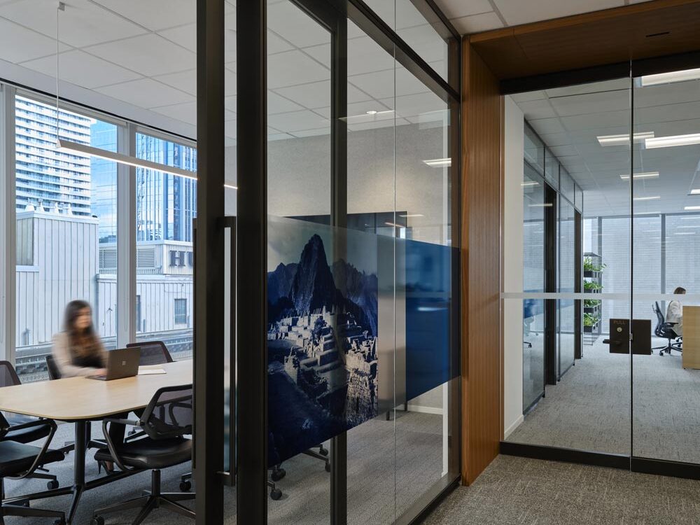 A view into a boardroom through glass wall, adjacent to a glass double door leading to more work stations