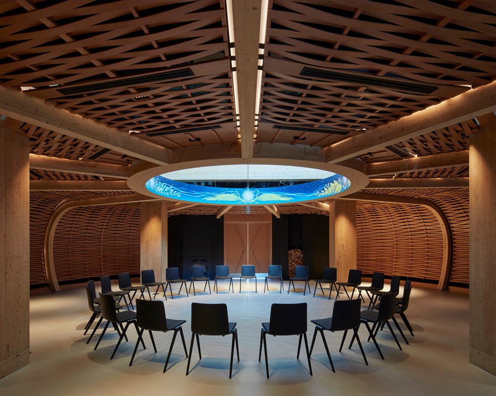 A circular room where walls are amde of a basket-like weave with chairs set up in a circle in the centre. In the centre of the ceiling is a circular opening