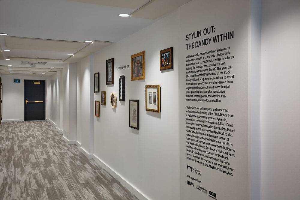 A white gallery wall in a hallway with small framed pictures and some text written on the wall