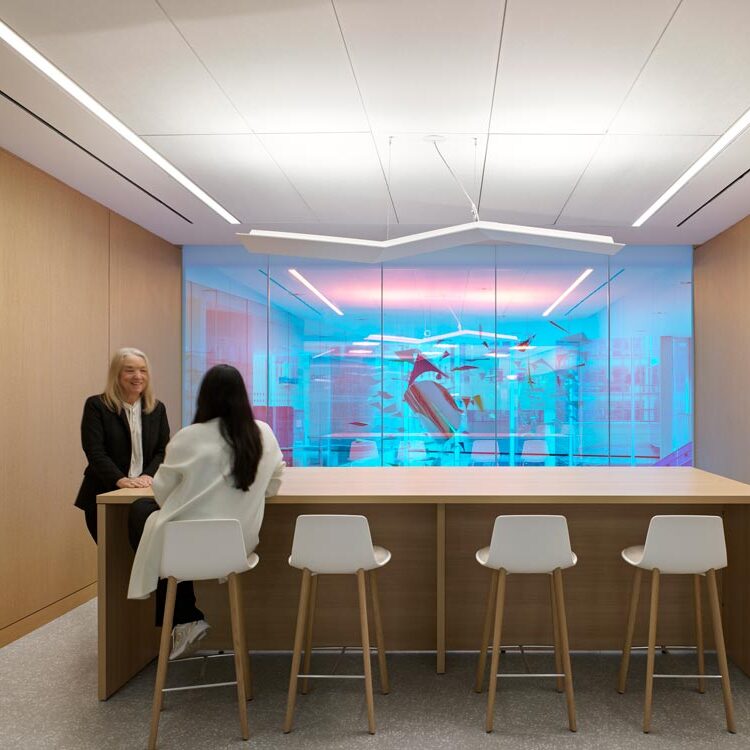 The mobile installation is visible through the blue-hued glass on the second level from this lounge space with high table and bar stools