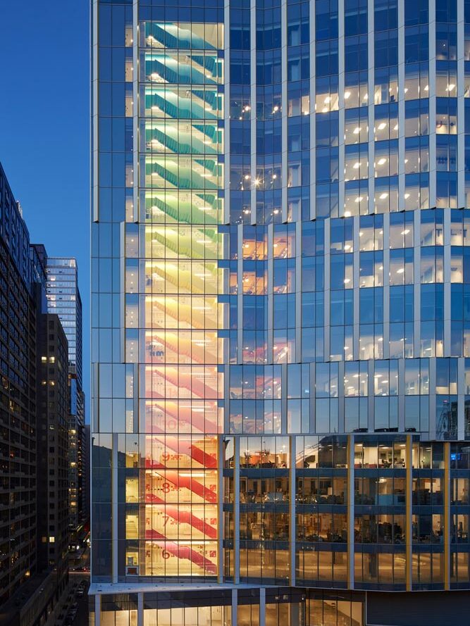 Rainbow staircase visible through the building's glass from the street. Each floor is one colour