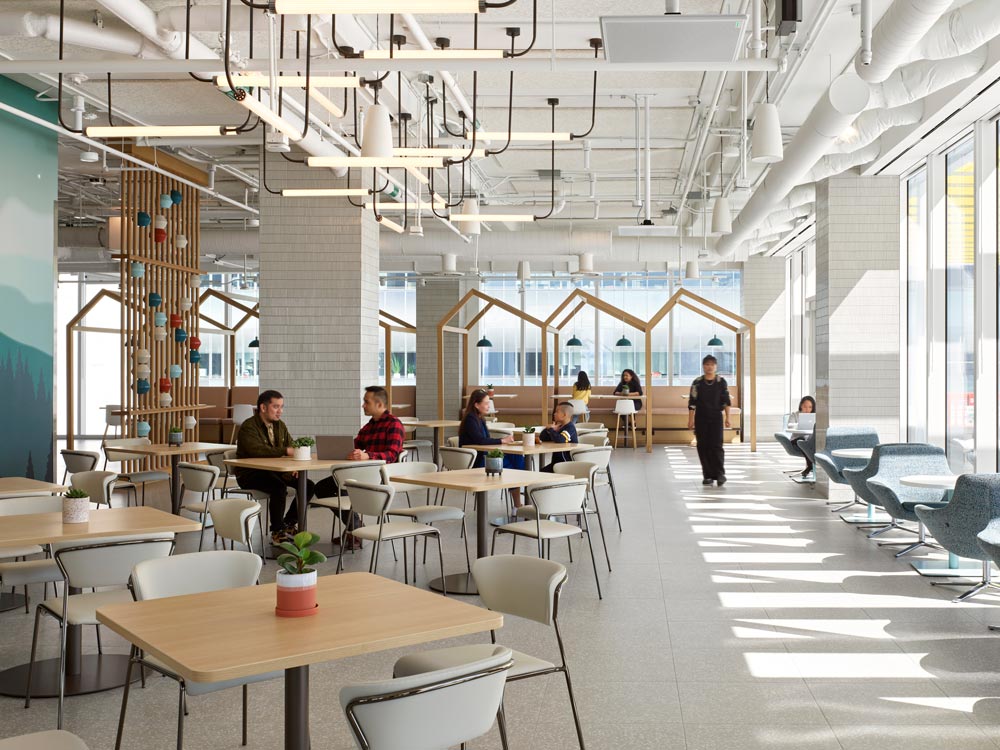 Rooftop workspace with high, loft-style ceilings and an interesting industrial linear light fixture above many smaller tables for people to work or hang out. 