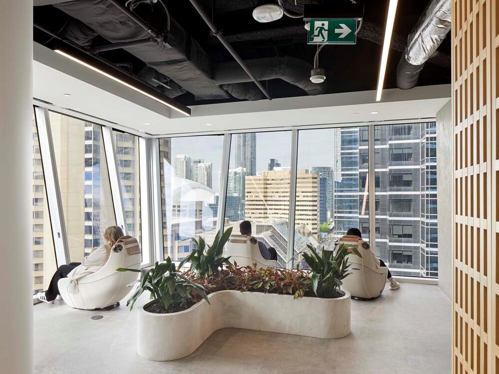 A lounge area with comfy chairs turned toward the floor to ceiling windows looking onto the city views