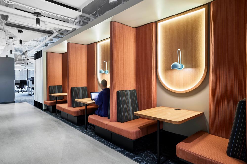 A quiet area with small booths off of the wall upholstered in teracotta coloured fabric.