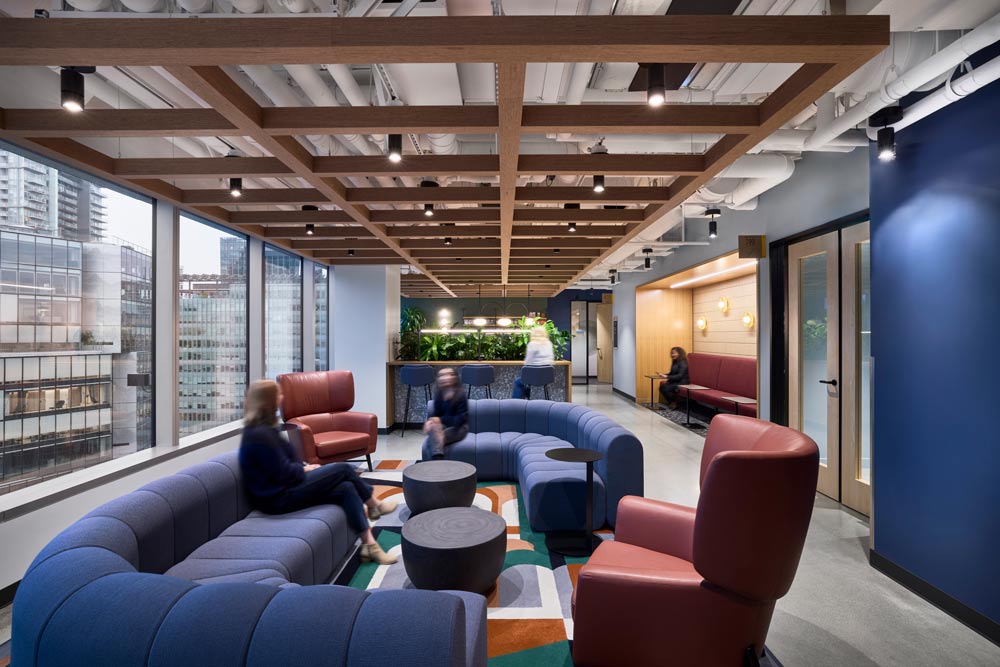 Lounge area with sofas in blue and burgundy next to a large window looking onto the downtown buildings