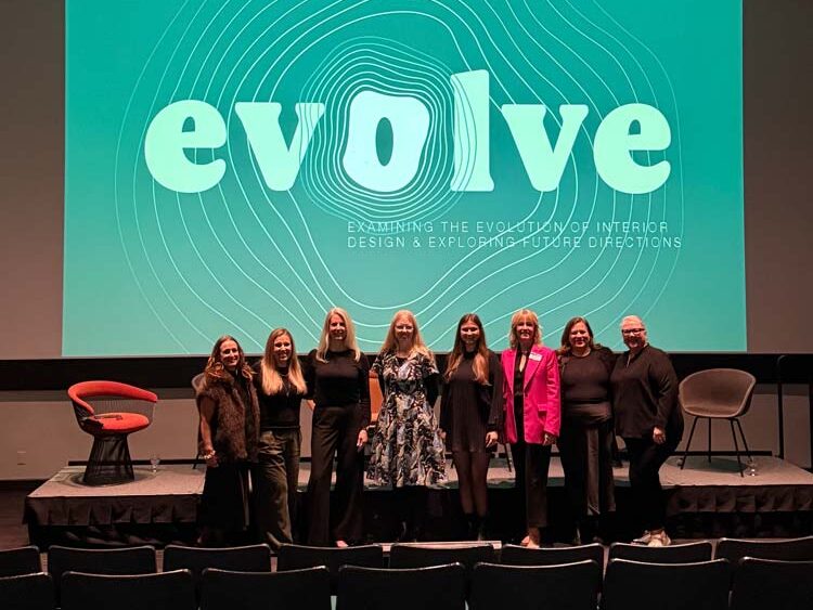 Panelists standing in front of the stage before the event, the title of the event is displayed behind them on the screen - 'Evolve'