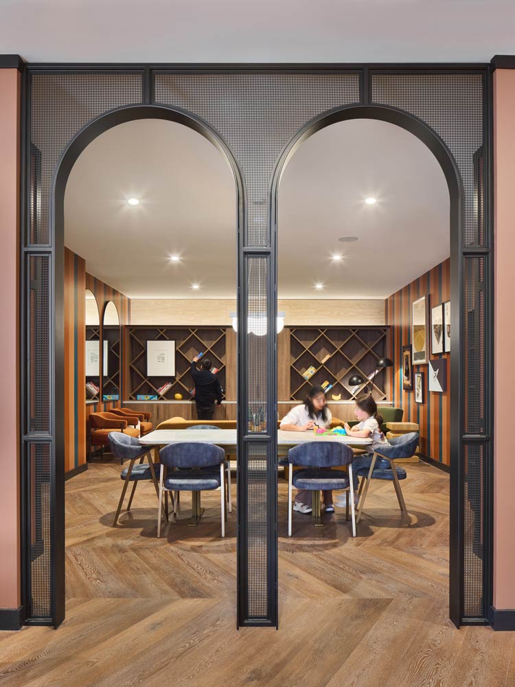 A multi use room with a large table in the centre and diagonal shelving in the back, meant for crafting, reading, hanging out. The entrance to the room is made of 2 metal arches