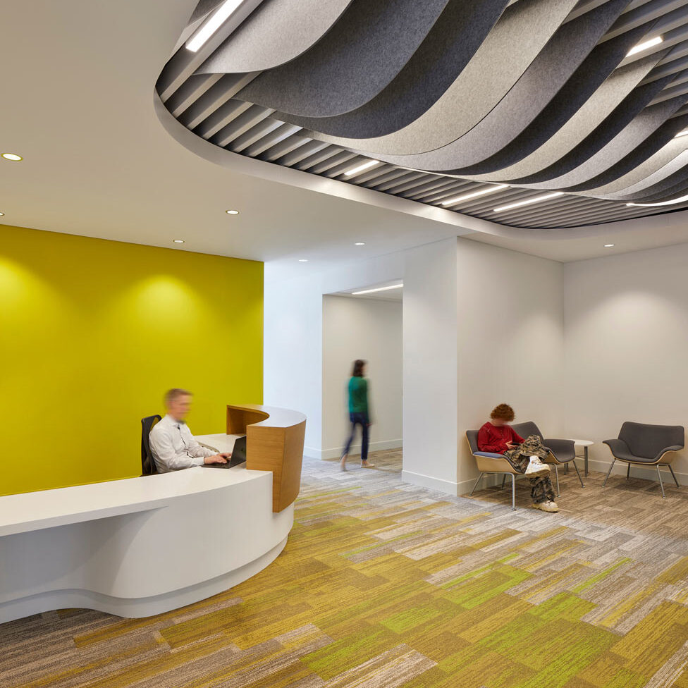 Faculty office reception with wavy feature hanging from the ceiling, and underneath it is a white and wood finish curved reception desk