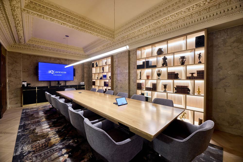 A board room with a a long conference table and built in lit-up modern shelving in the wall, while above is the original plaster detailing