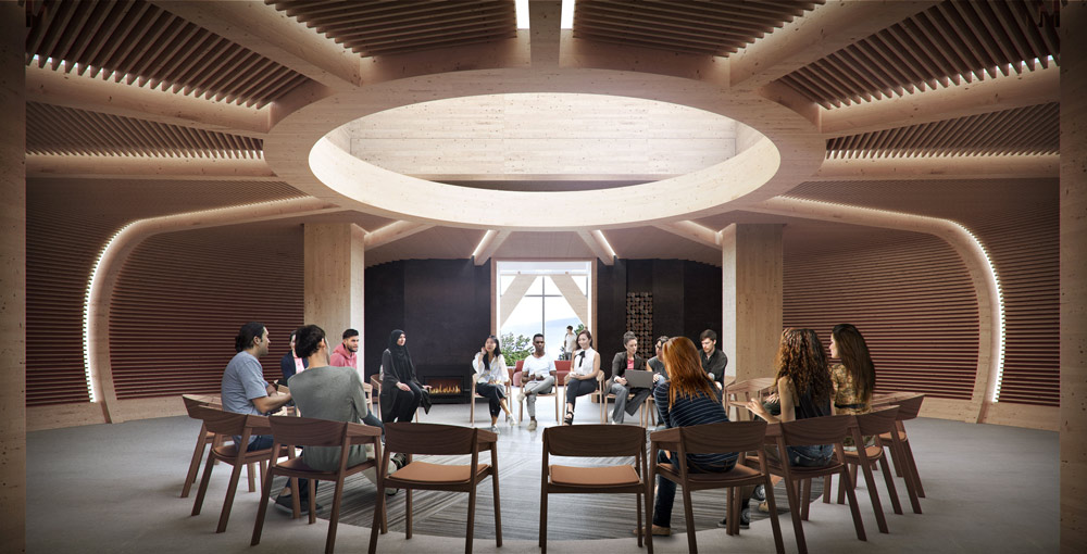 A circular room where walls are made of a basket-like weave with people sitting on chairs set up in a circle in the centre. In the centre of the ceiling is a circular opening