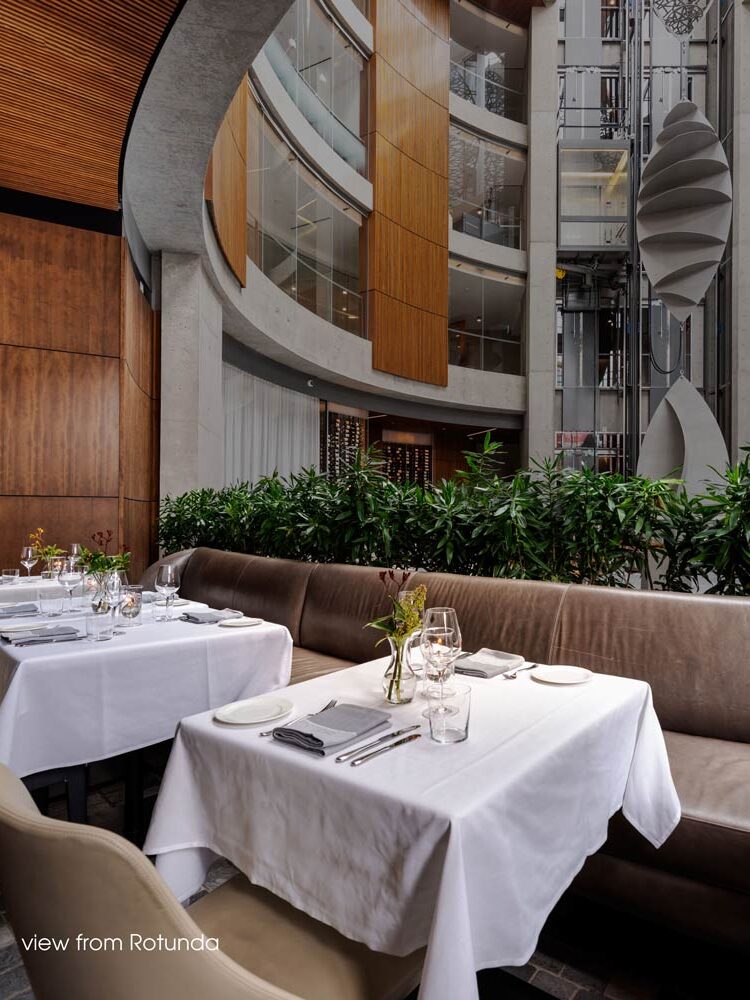 The view of the central Rotunda, showing two dining tables and behind them greenery that separates the dining area from the central rotunda area