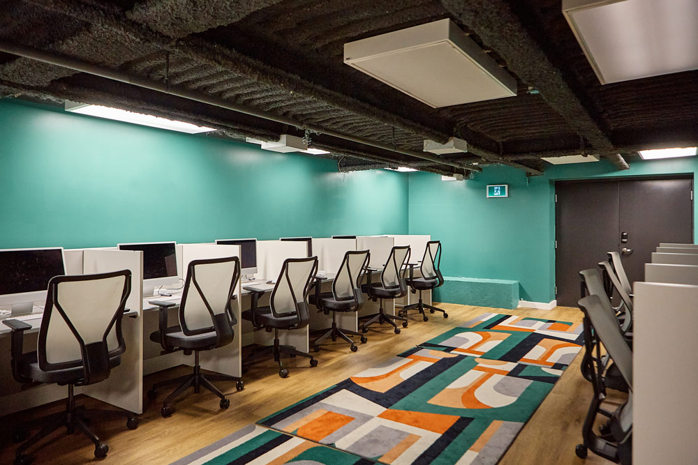 A room in the basement with modern workstations, and the colour scheme is predominantly green, with some orange and black accents.