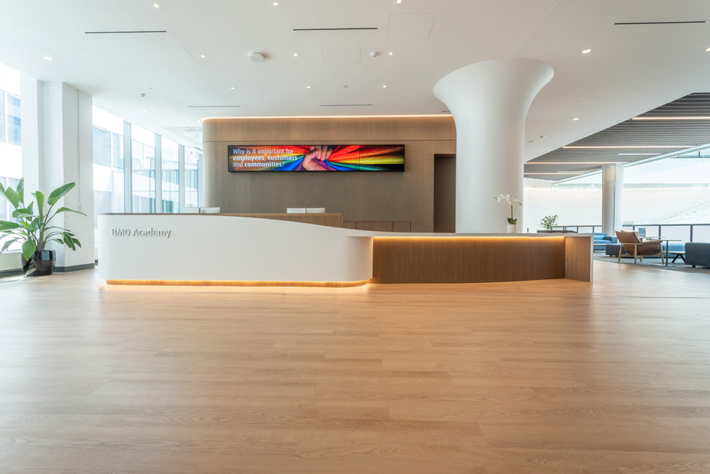 Reception desk area in a neutral pallete, wood and white, and a colourful branded screen on the wall behind the desk adds colour