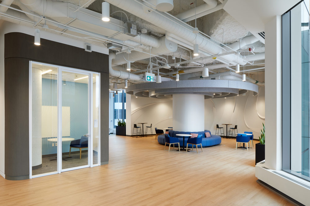 A central hallway showing a central lounge and social area around a big column that acts as the focal element. A small private room is seen on the right side, for quiet studying