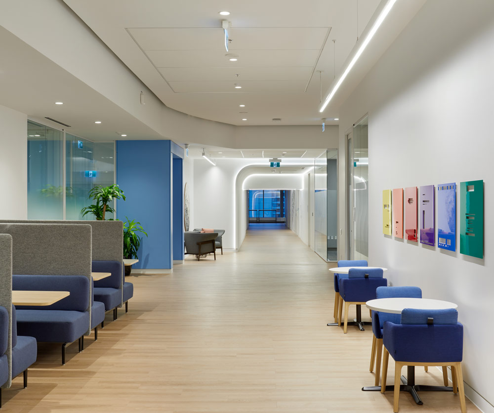 A wide hallway with seating booths on one side and small tables for two on the other. The accent colour blue dominates in this area