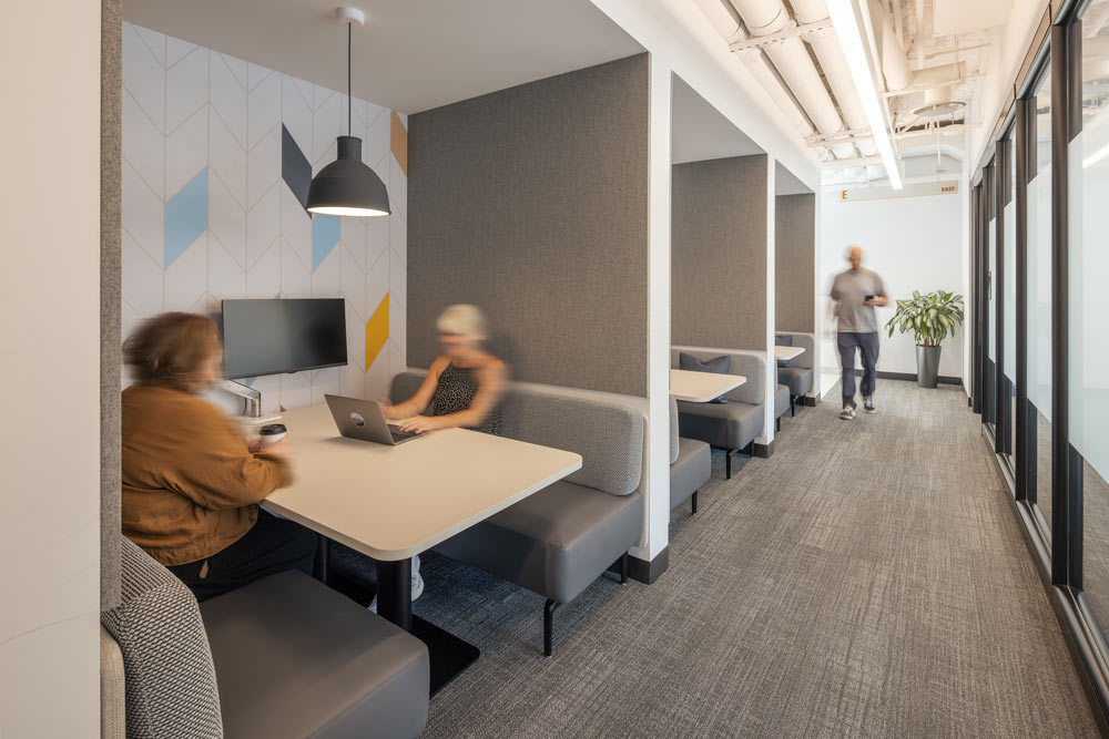 A view of a hallways along which there are a few booths with desks and benches meant for work and meetings