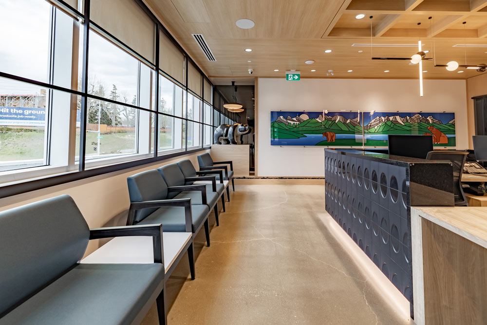 A view of the reception waiting area with chairs placed under the windows across from the desk, and a colourful indigenous themed art work on the long white adjacent wallwall 