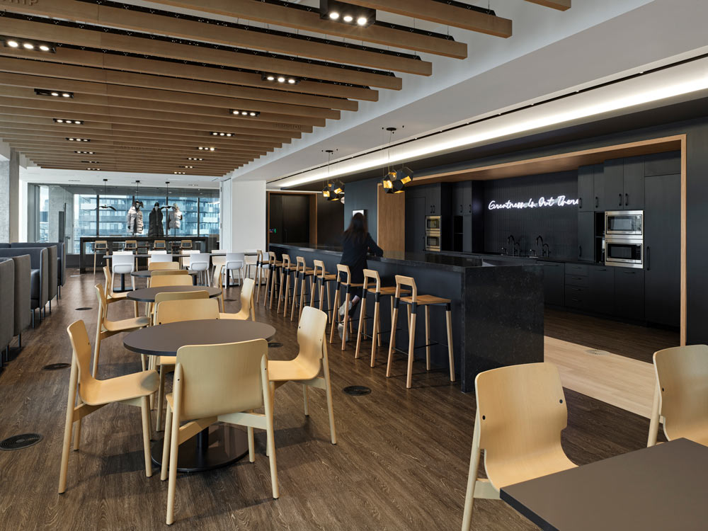 Cafeteria and kitchen area in predominantly black and light wood finishes. The kitchen is completely in black with a neon sign on the wall above the sink area