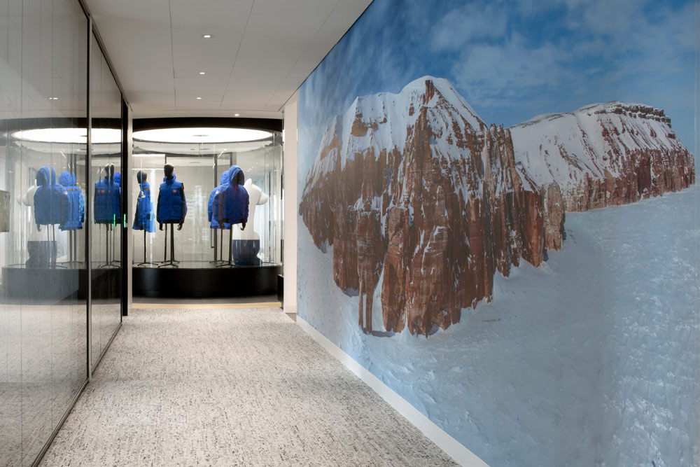 A wall mural showing a snowy mountain in a hallway that leads toward a circular glass display with jackets on mannequins