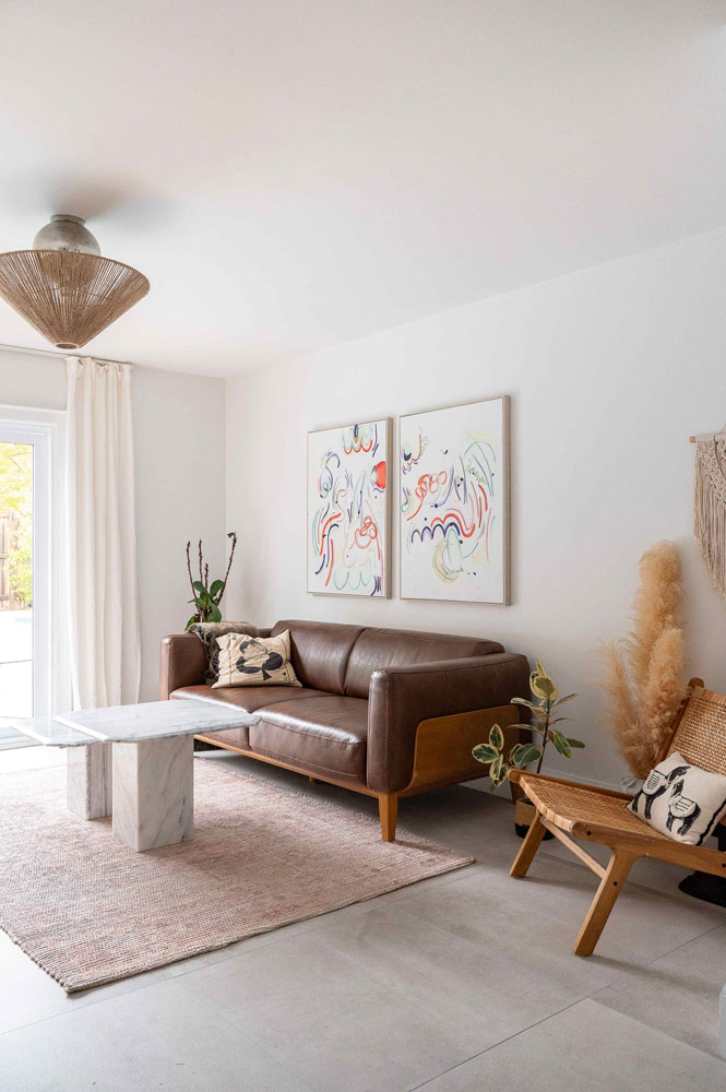 Living area with a dark brown leather counch against a marble coffee table, and abstract art above the couch