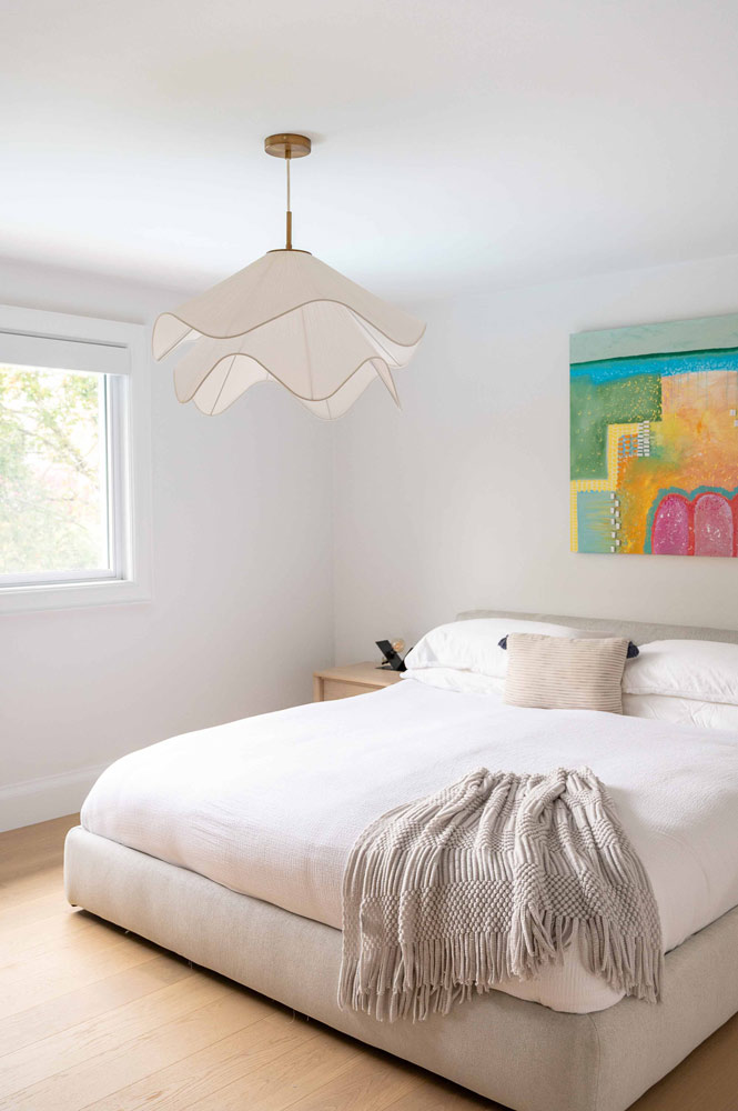Minimalistic bedroom, with the white bed against a white wall with a colourful piece of art hanging above