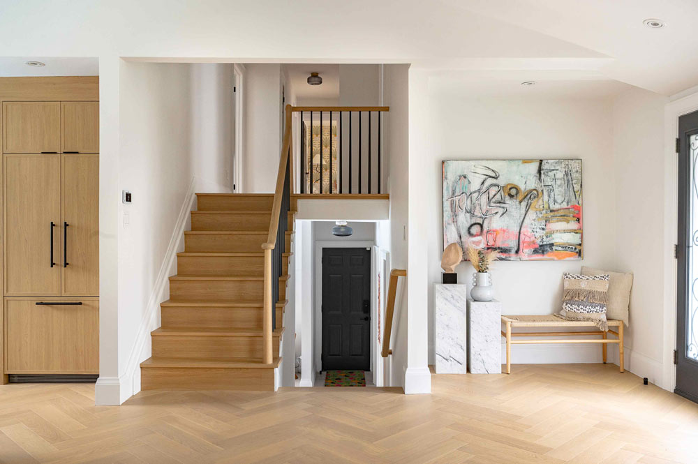 Foyer and staircase leading to the upper floor. A colourful abstract art piece hangs on the wall to the right and the kitchen cabinets are visible to the left