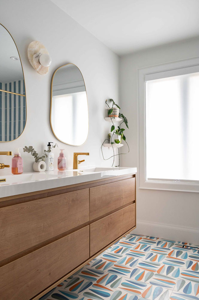 main bathroom with floor tile in colourful geometric pattern and wooden floating double vanity and two organic mirrors above the sinks