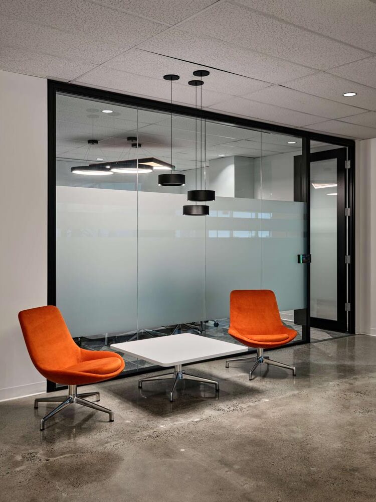 Waiting area in the reception with two orange lounge chairs and one coffee tables, and a modern pendant ligh fixture hangs above