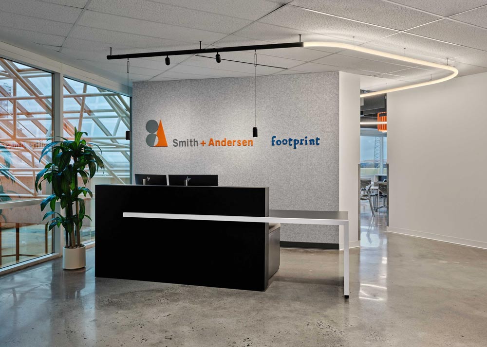 Reception area with a linear modern black reception desk, in front of a grey wall with the Smith + Andersen branding on it