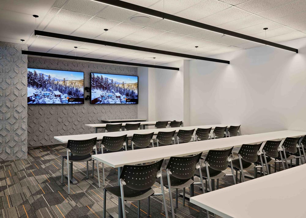 Space with long tables in a few rows in front of 2 large TVs, rand acoustic paneling on the wall where the TV's are hanging